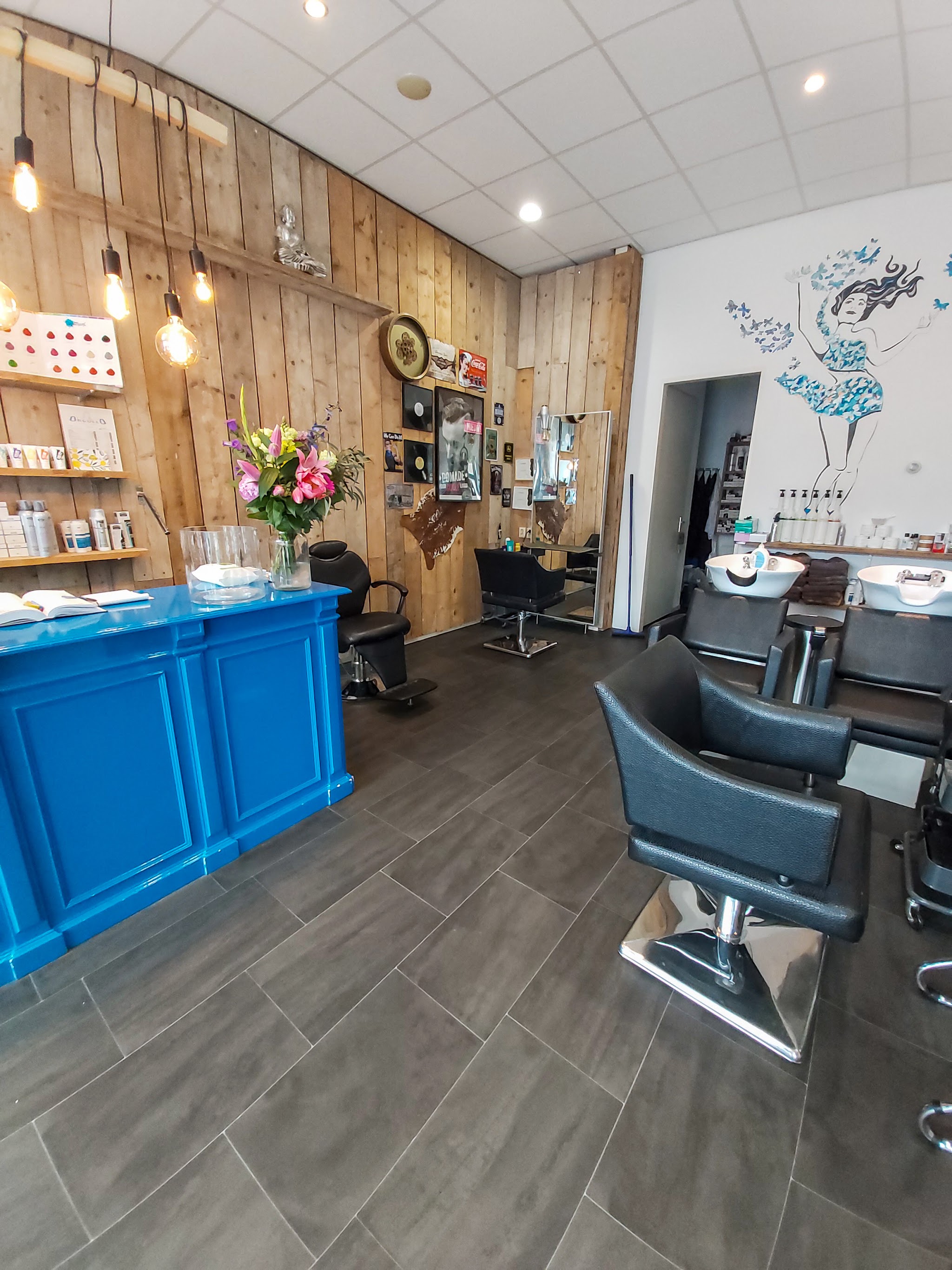 De salon met blauwe balie, houten wand en kapperstoelen